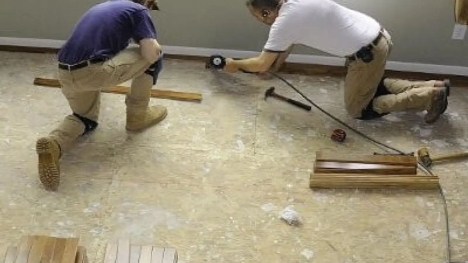 Two technicians kneeling on a subfloor to remove and replace damaged flooring during a water damage repair